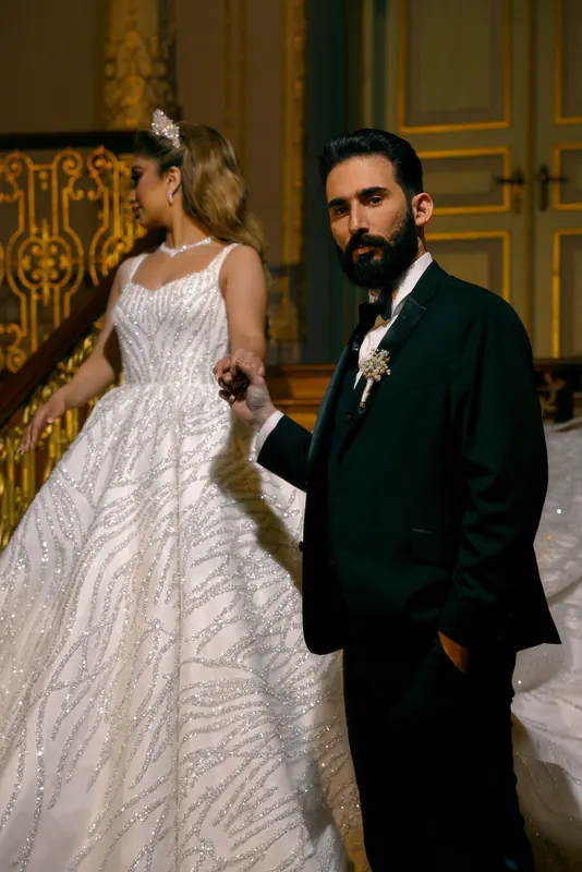 Groom holding the bride's hand on a gilded staircase