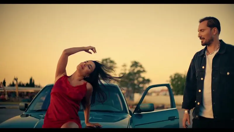 Woman in red dancing by a car at sunset