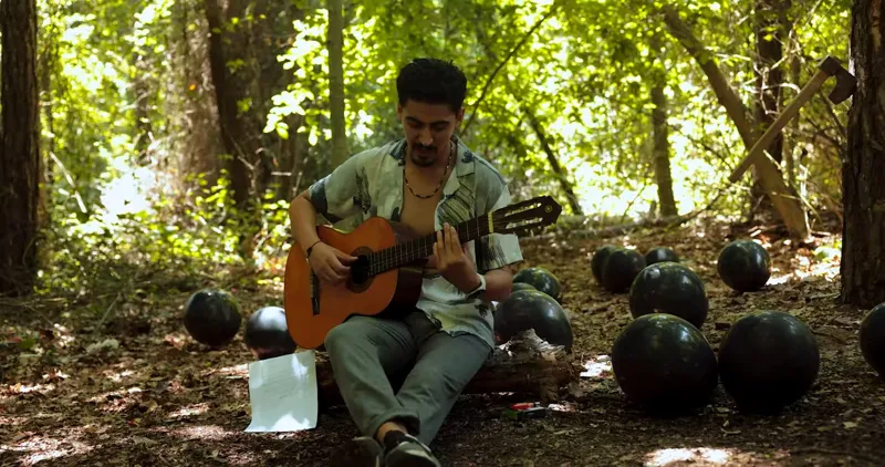 Saqer Almilady playing guitar among black balloons in a forest